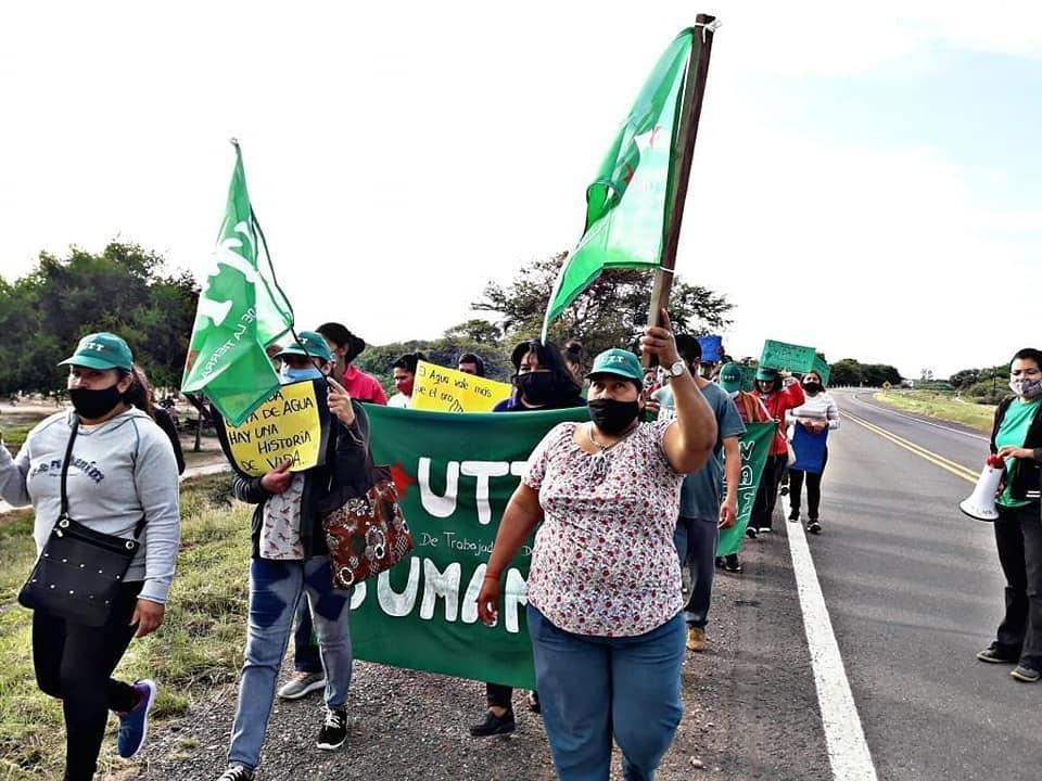 Integrantes de una organización social participan en una caminata por el agua portando banderas y carteles.